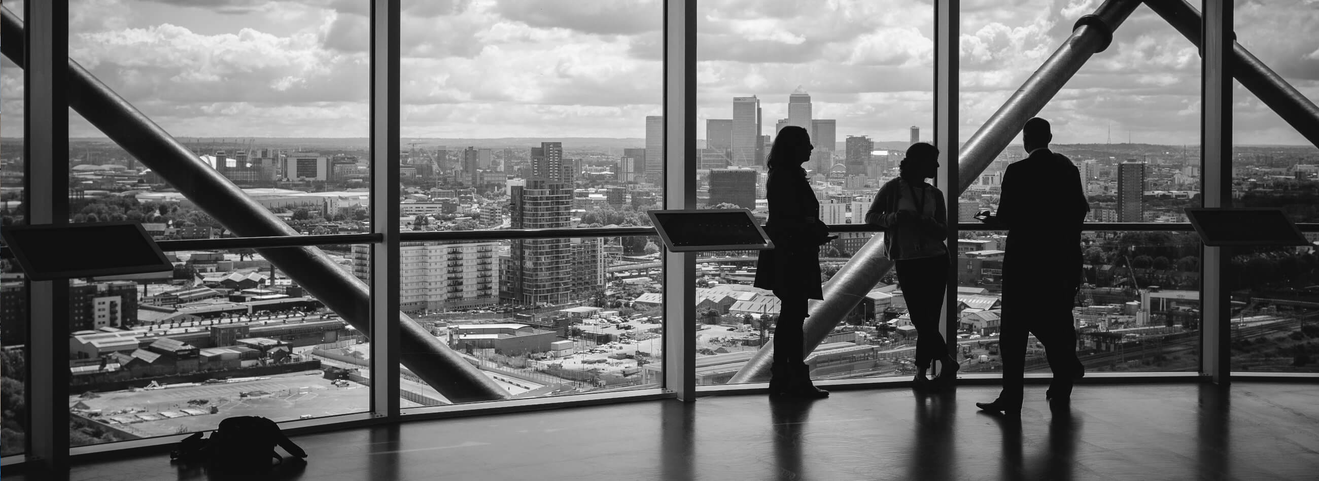 three people overlooking the city from inside a glass wall building